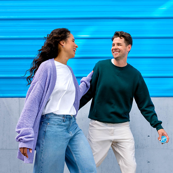 A woman and a man walking and looking at each other, while the man is holding a can of ZYN nicotine pouches